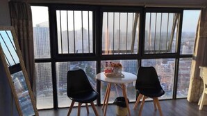 A room with a large window, two chairs, a small table with a vase and books, and a bed. - Chuzhou Aidi Daily and Short-Term Rental Luxury Apartment (Chuzhou)