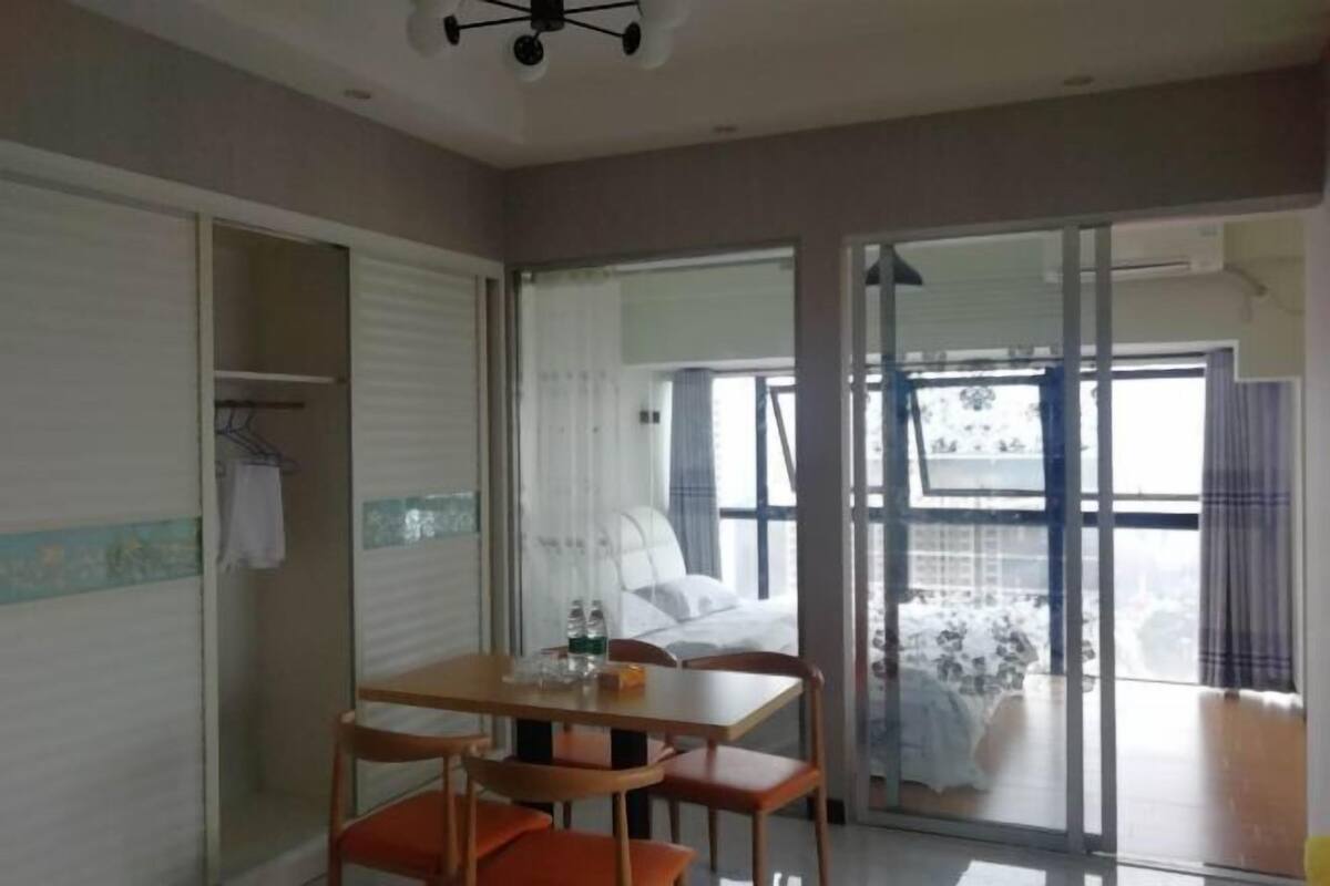 A hotel room with a bed, a table with chairs, a sliding glass door to the balcony, and a closet with a hanging rack.