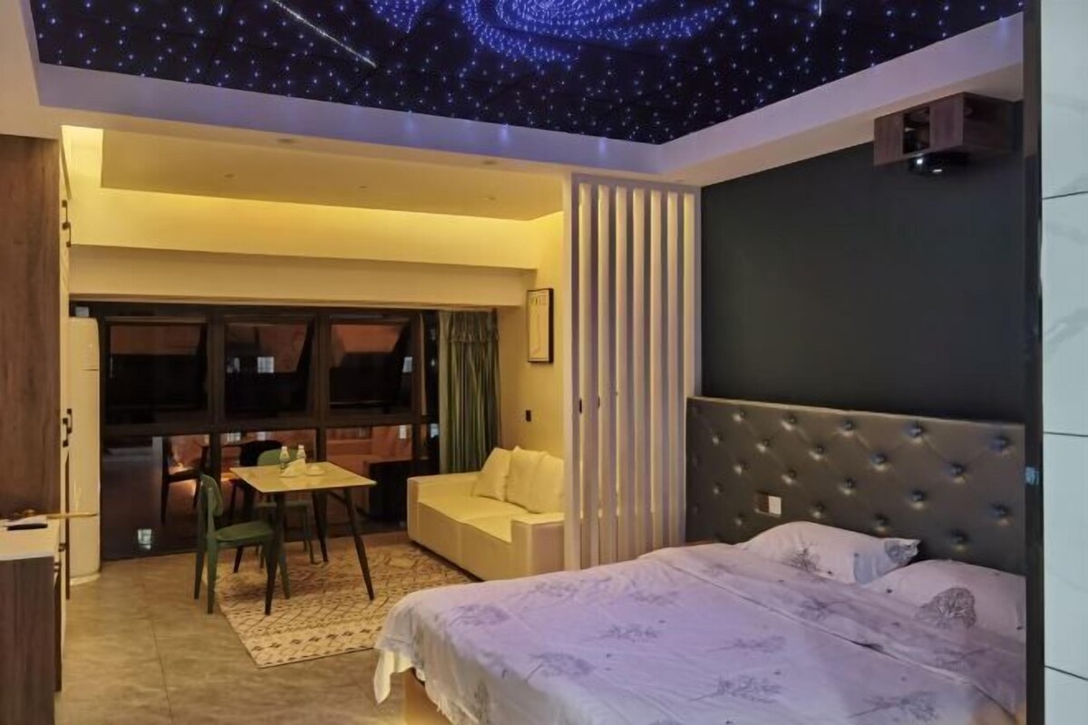 A bedroom with a bed, a desk, a chair, a sofa, and a view of the outside.
