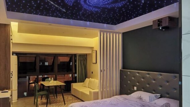 A bedroom with a bed, a desk, a chair, a sofa, and a view of the outside. - Chuzhou Aidi Daily and Short-Term Rental Luxury Apartment (Chuzhou)