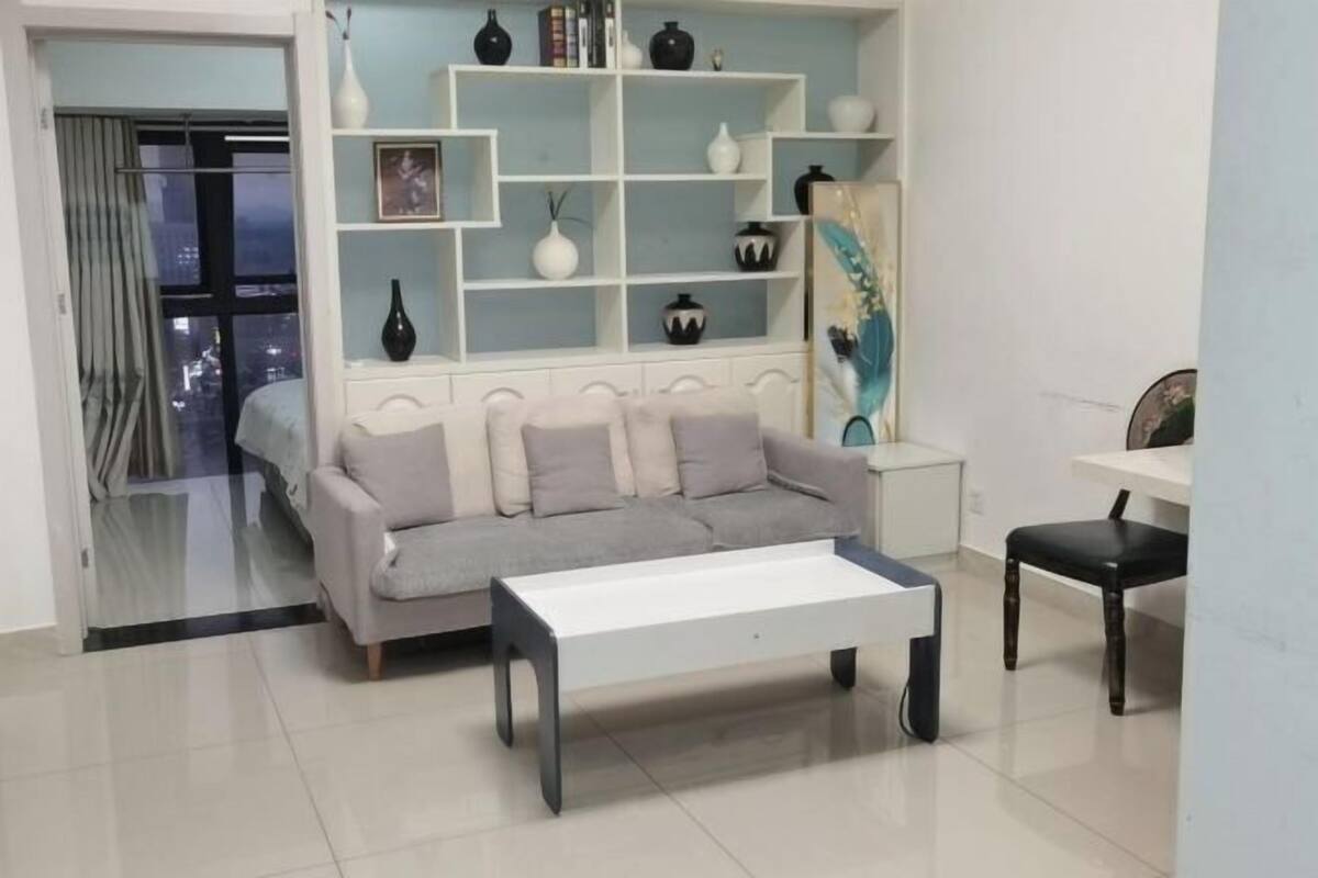 A modern living room with a sofa, a coffee table, a bookshelf, and a view of the city through a window.