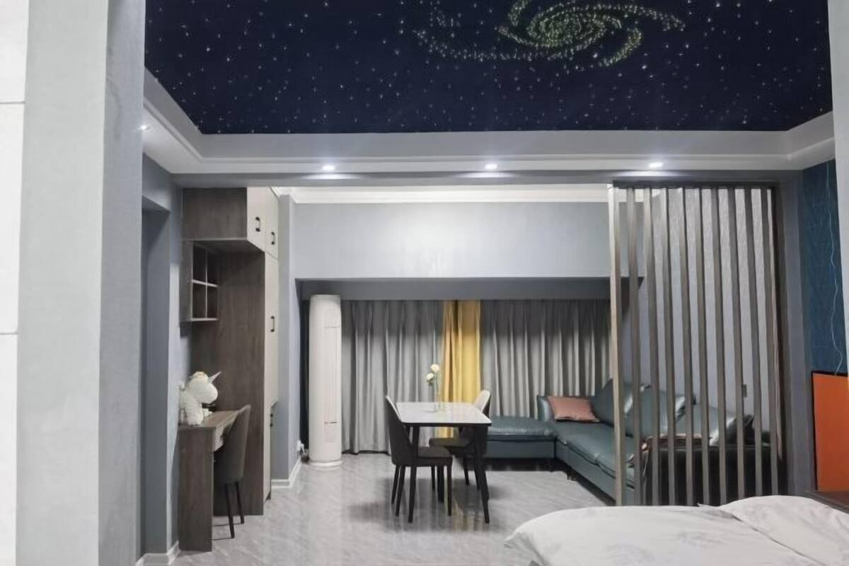 A hotel room with a starry ceiling, a dining area, a sofa, and a bed.