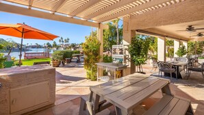 An outdoor patio area with wooden tables and chairs, a large orange umbrella, and a view of a lake. - Beautiful sunset Lakehouse with with amazing views and heated pool and jacuzzi ! (Avondale)