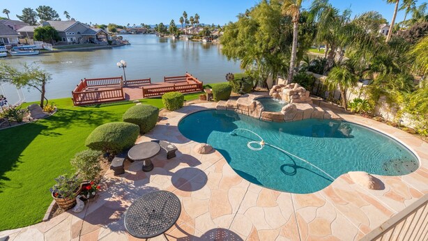 A swimming pool with a view of a lake, surrounded by palm trees and a patio area with seating. - Beautiful sunset Lakehouse with with amazing views and heated pool and jacuzzi ! (Avondale)