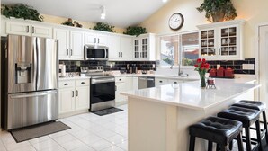 A modern kitchen with white cabinets, stainless steel appliances, a central island with bar stools, and a clock on the wall. - Beautiful sunset Lakehouse with with amazing views and heated pool and jacuzzi ! (Avondale)
