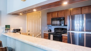 A kitchen with wooden cabinets, a stainless steel refrigerator, a microwave, and a stove.