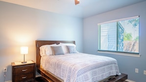 A bedroom with a bed, bedside table, lamp, and window with blinds.
