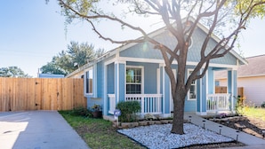 A single-story house with a blue exterior, a wooden fence, a tree in the front yard, and a driveway.