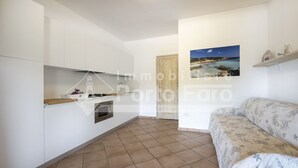 Een moderne keuken met witte kasten, een ingebouwde oven en een magnetron. Er is een houten aanrecht en een deur die naar een andere kamer leidt. Een bank met een bloemenprint staat op de voorgrond.