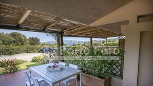Een overdekt terras met een tafel en stoelen, een houten pergola en uitzicht op een weg en groen.