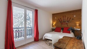 Ein Schlafzimmer mit einem hölzernen Kopfteil, einem Bett mit roten Kissen, einem Holztisch und Blick auf schneebedeckte Bäume durch eine Schiebetür.