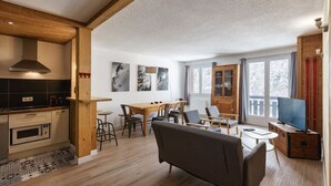 Eine moderne Küche mit eingebautem Backofen und Mikrowelle, ein Essbereich mit Holztisch und Stühlen sowie ein Wohnzimmer mit Sofa und Fernseher.