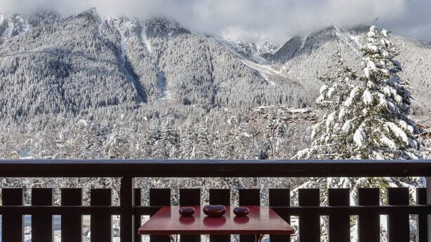 Aussicht auf Berge mit schneebedeckten Bäumen und einem Tisch mit zwei Tassen.