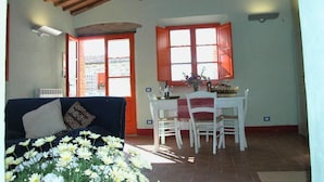 A dining area with a wooden ceiling, white walls, and red-framed windows. - Apartment With Beautiful View in the Crete Senesi (Asciano)