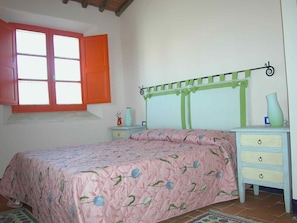 Quarto com cama, mesa de cabeceira, cômoda, janela com persianas laranja e cabeceira verde.