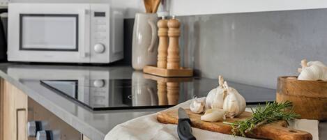 A kitchen with a microwave, wooden cutting board, garlic, a knife, and a wooden bowl.