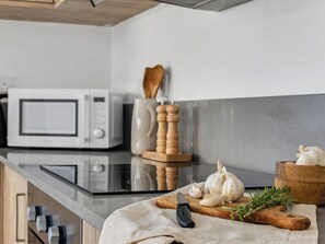 A kitchen with a microwave, wooden cutting board, garlic, a knife, and a wooden bowl. - Sanders White Mountains (Tremithousa)