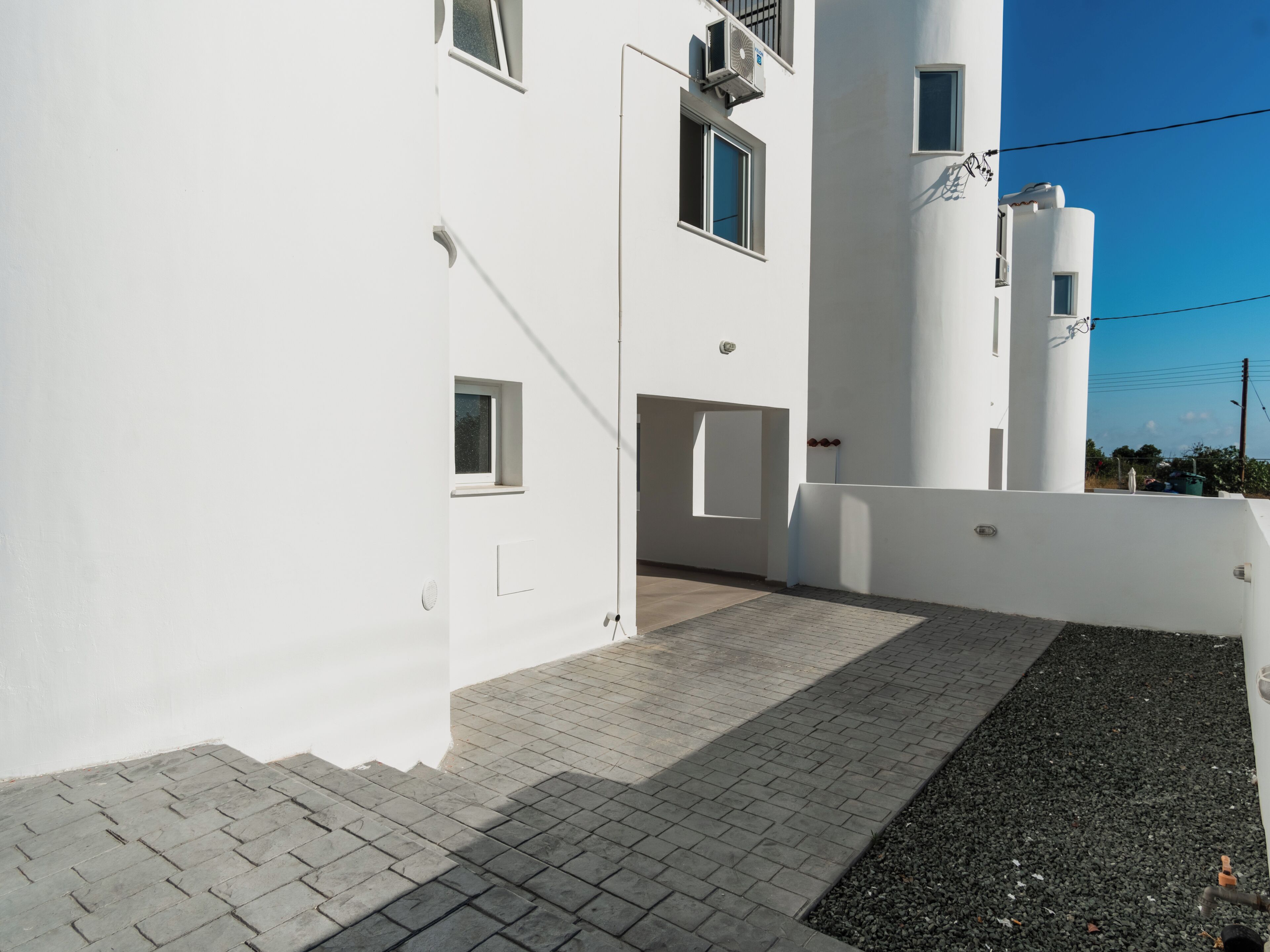 Un edificio moderno con fachada blanca, acceso pavimentado y cielo despejado.