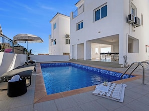 A swimming pool with a tiled deck, lounge chairs, and a covered seating area.
