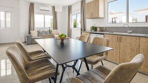 Une cuisine moderne avec des meubles en bois, une table à manger noire et un coin salon comprenant un canapé et des fauteuils.