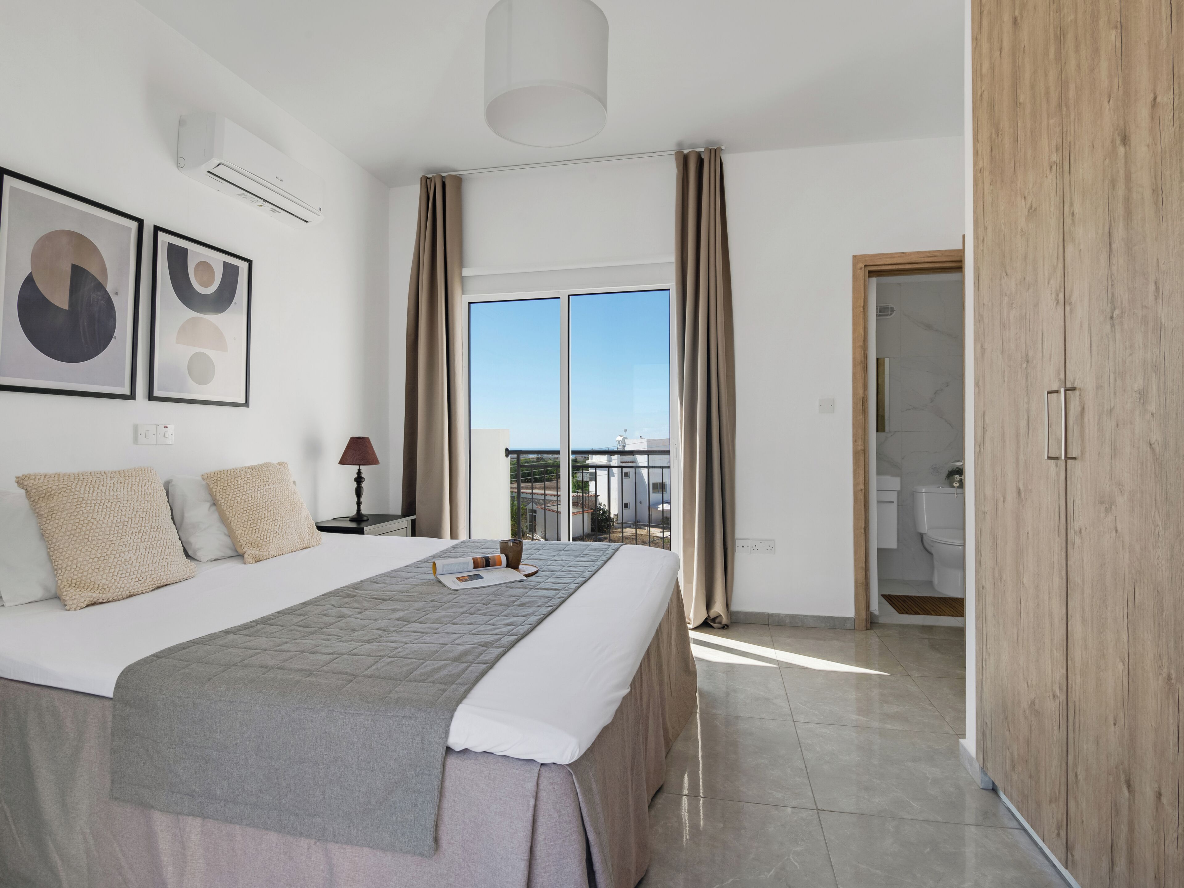 A modern hotel room with a large bed, a view of the city, and a wooden wardrobe.