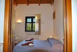 A bedroom with a bed, a chair, a window with curtains, a radiator, and a wall-mounted light fixture.