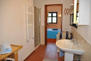 Une salle de bain avec une douche, un lavabo et un lit à l’arrière-plan.