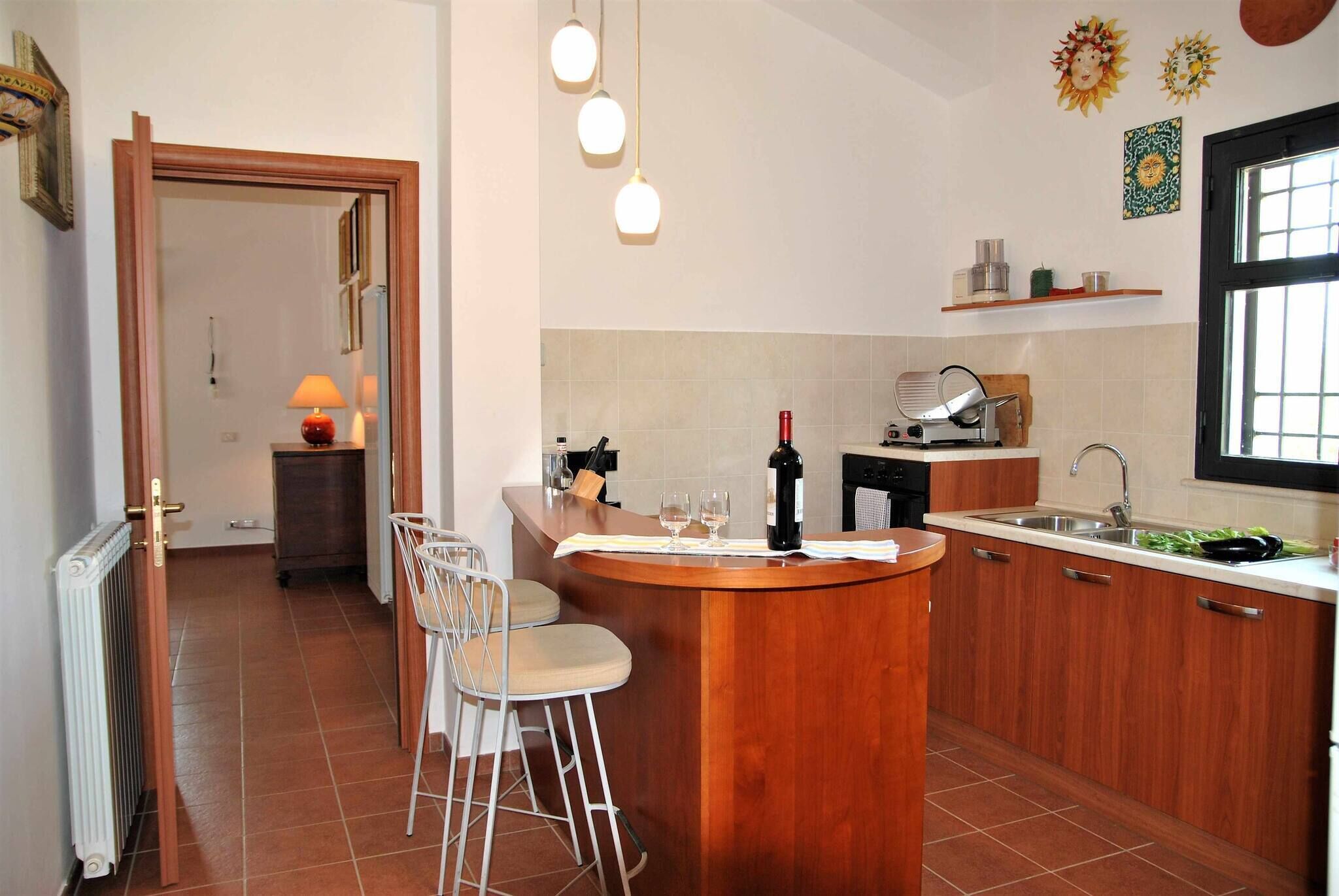 Una cocina con una isla de madera, taburetes de bar, un lavamanos y un ventanal.