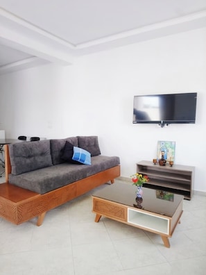 A living room with a sofa, coffee table, TV, and a small shelf with decorative items. - Second Position Beach Dar Allouche Kélibia Rfi Rdc (Dar Allouche)