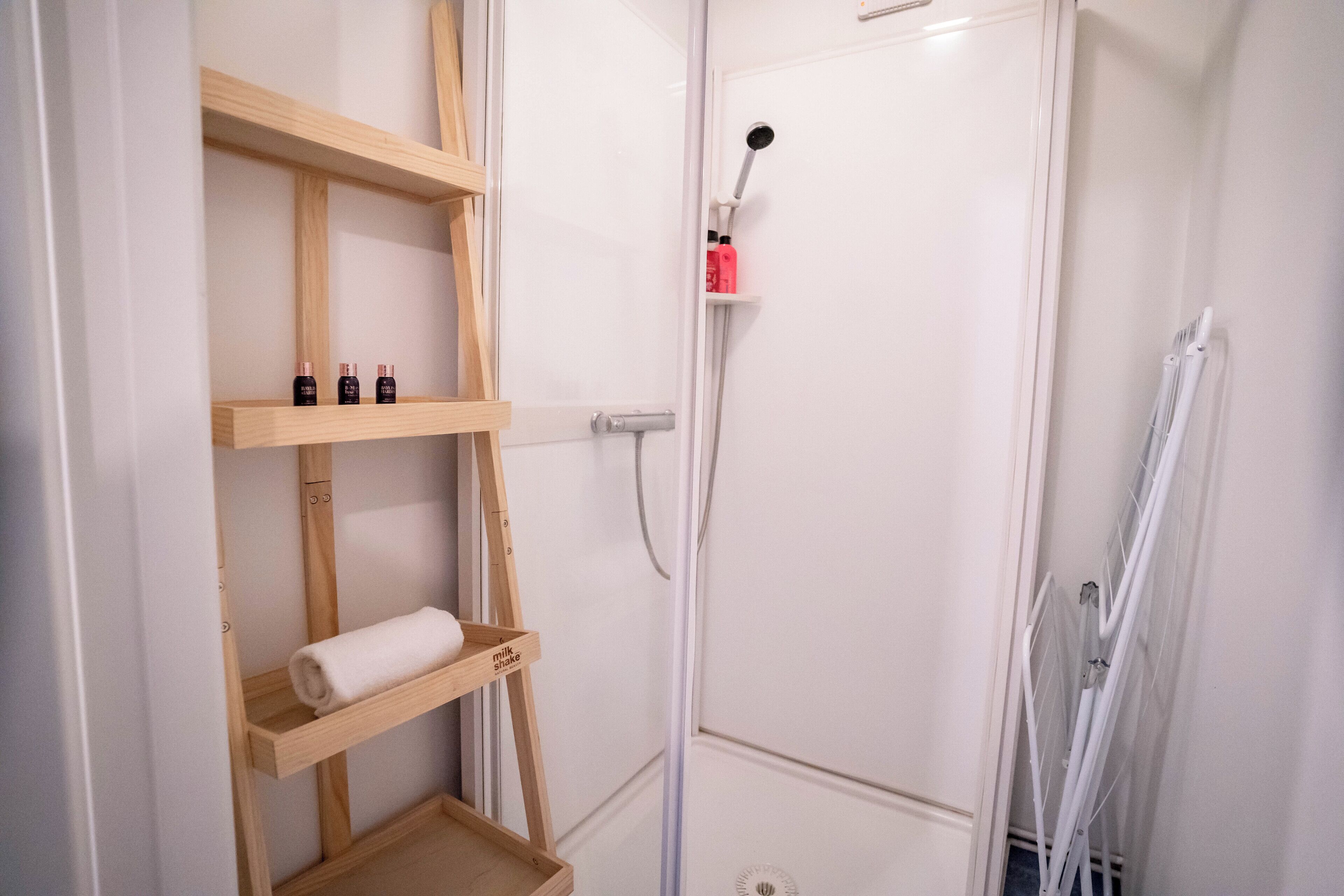 Een douche met handdouche, een witte deur en houten planken met toiletartikelen.