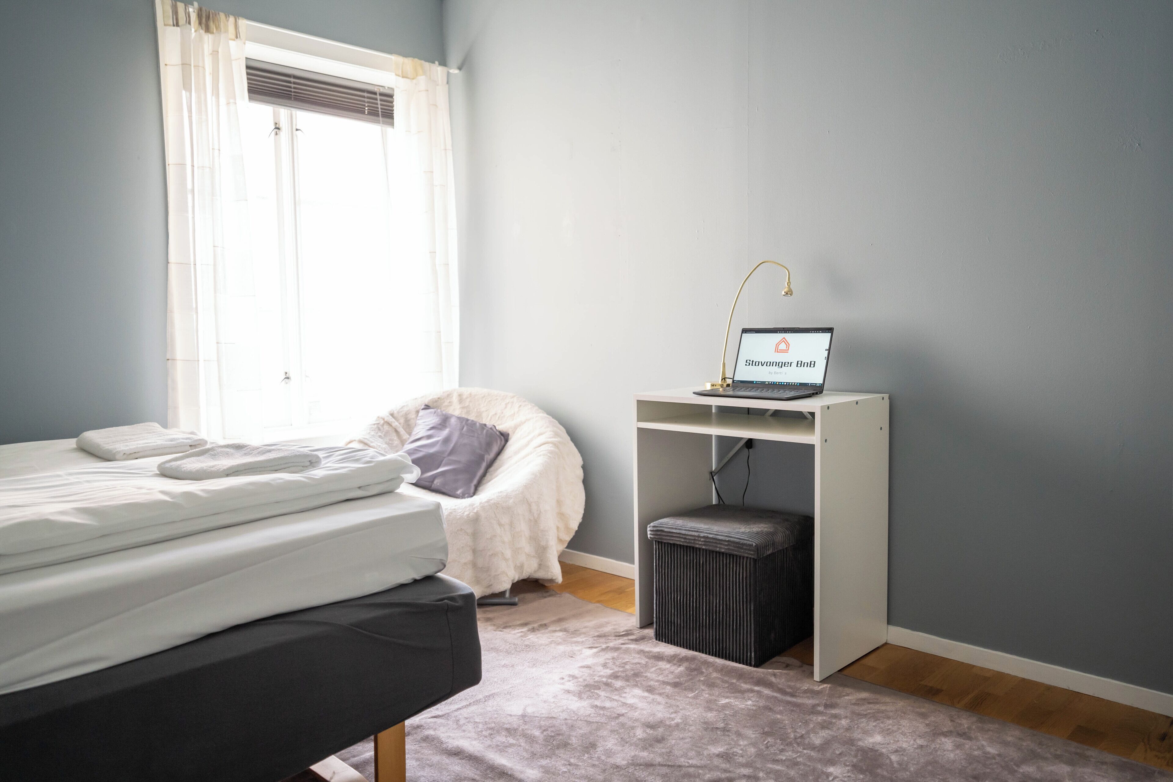 Un dormitorio con una cama, un escritorio con una computadora portátil, una silla y una ventana con cortinas.