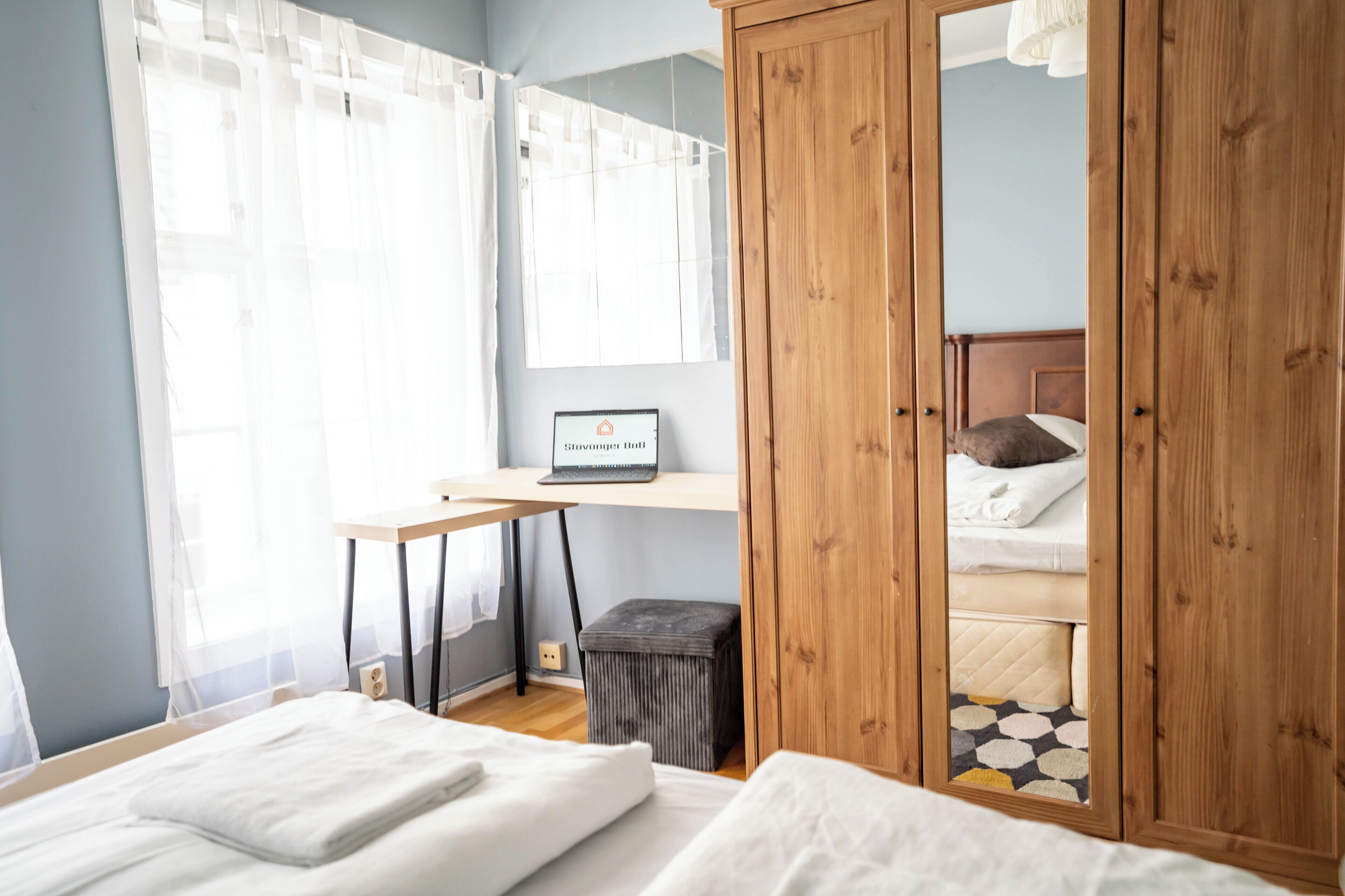 A bedroom with a bed, a desk, a computer, a wardrobe, and a window with curtains.