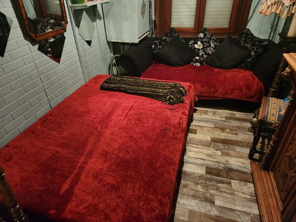 A room with two beds covered in red blankets, a wooden floor, and a brick wall.