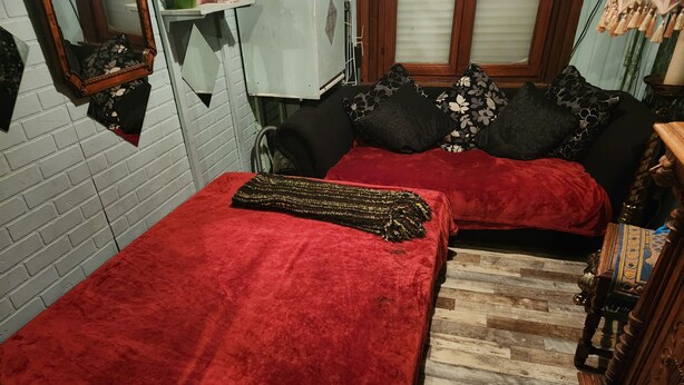 Una habitación con dos camas cubiertas con mantas rojas, suelo de madera y pared de ladrillo.