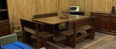 Een kamer met een houten eettafel, bankjes, een kleine bank, een lamp, een televisie en een kast.
