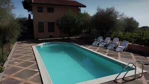 A rectangular swimming pool with a tiled deck, surrounded by lounge chairs and a building with a tiled roof in the background. - Magnificent Villa Between Etna and the sea With Breathtaking Views of Mount Etna (Linguaglossa)