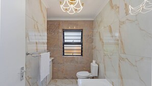 Une salle de bain avec des murs en marbre, des toilettes, une baignoire, un porte-serviettes et une fenêtre avec un store.