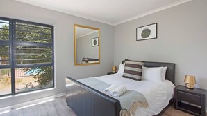 Une chambre à coucher avec un lit, des tables de chevet, une fenêtre et un miroir.