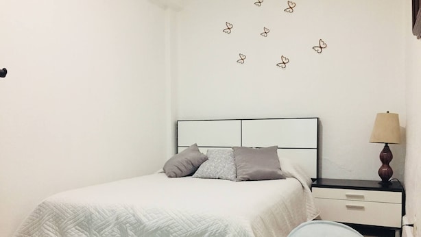 A bedroom with a bed, a nightstand, a lamp, and a wall decoration of butterflies. - Department, Studio Type Excellent Location (Mexico City)