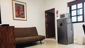 A living room with a brown sofa, a refrigerator, a microwave, a door, and a framed picture on the wall. - Department, Studio Type Excellent Location (Mexico City)