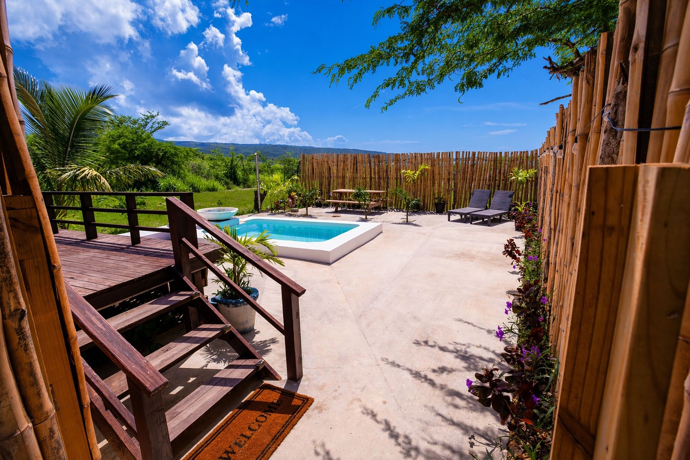 Ein Poolbereich mit Holzterrasse, Willkommensteppich und Bambuszaun.