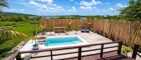 Una terraza de madera con un jacuzzi, sillas de descanso y vista a un lago.