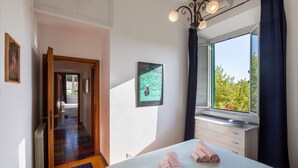Une chambre d’hôtel avec un lit, une fenêtre donnant sur un paysage agréable, une porte menant à une autre pièce et un tableau encadré au mur.