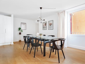A modern dining area with a glass table, black chairs, a hanging light fixture, and framed artwork on the wall.