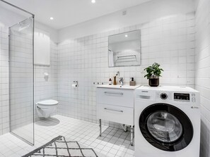 A modern bathroom with a glass shower enclosure, a toilet, a sink with a mirror, and a front-loading washing machine. - City 1- Pleasant 4-bdr Apt in Central Copenhagen (Copenhagen)