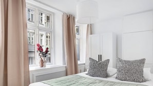 A bedroom with a bed, a window with curtains, a vase with flowers, and a white wardrobe. - City 1- Pleasant 4-bdr Apt in Central Copenhagen (Copenhagen)