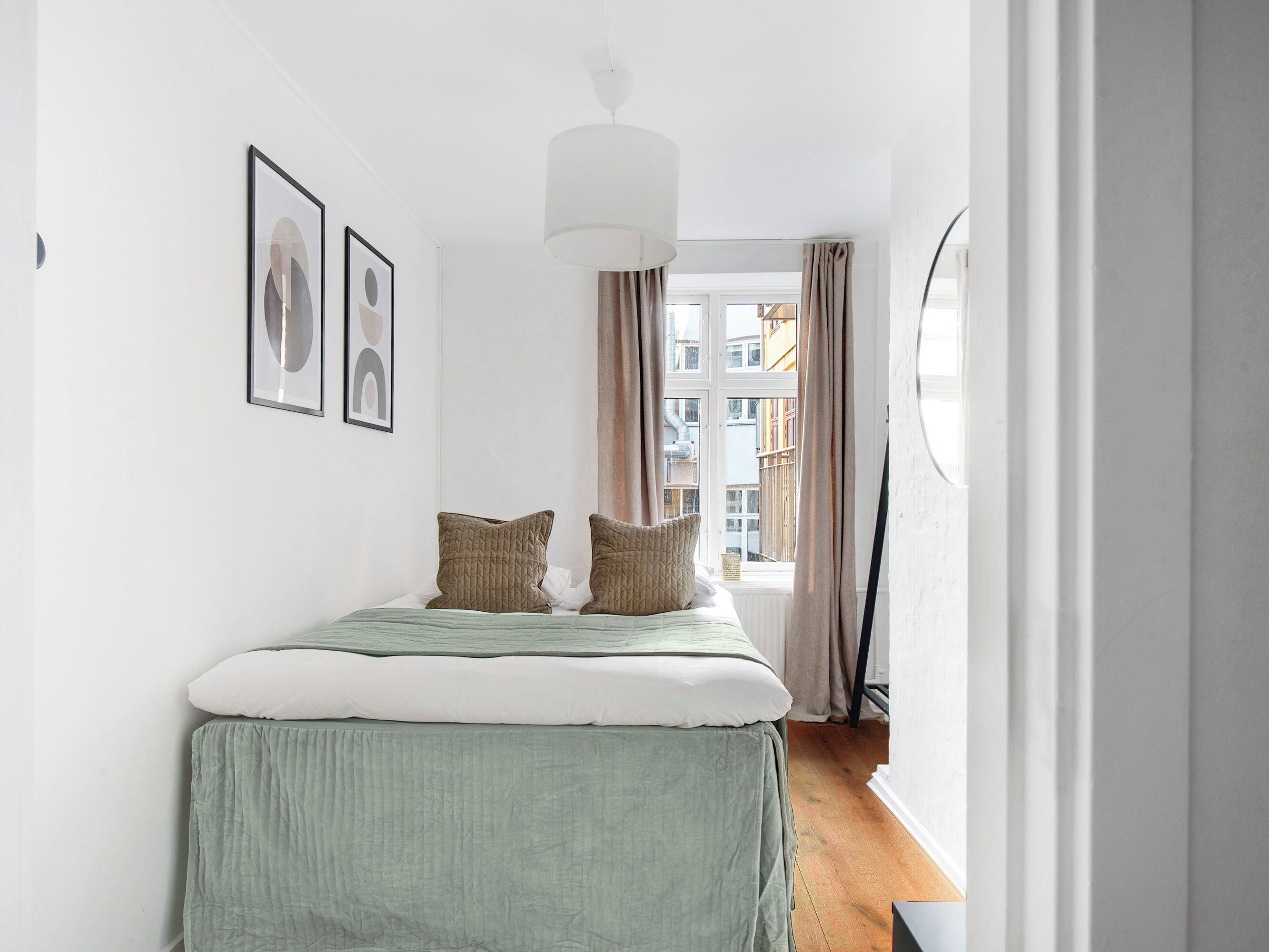 A bedroom with a bed, two pillows, a hanging light fixture, and a window with curtains.