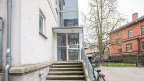 Un bâtiment doté d’un escalier extérieur menant à une entrée avec une porte en verre, un arbre et un vélo garé à proximité.