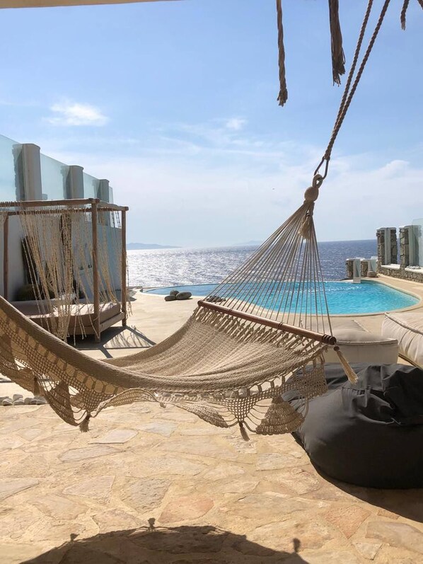 Un hamac installé près d’une piscine, avec un sol en pierre et des chaises longues.