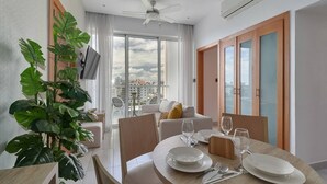 A modern dining area with a round table set for four, a large potted plant, and a city view through large windows. - Apartment N1001 Downtown Santo Domingo (Santo Domingo)